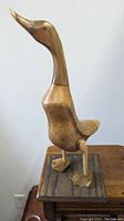 Side view of wooden gander duck sculpture on a square wooden base, showing natural wood grain and carved details