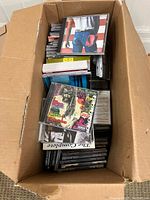 Photo showing a box filled with various CD jewel cases stacked and loosely packed, with several visible album covers.