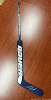 Full view of the blue Bauer goalie stick laying flat showing the Bauer logo on the shaft.