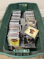 Green plastic tote filled with approximately 250 CDs in jewel cases. Visible CDs include artists Rascalz and Bruce Cockburn.