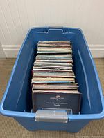 Blue plastic bin filled with a large collection of vintage vinyl records, showing the variety of the record covers and sleeves.