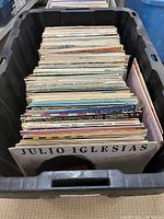 Overhead view of a black plastic bin filled with vintage vinyl records, showing diverse album covers and artists.