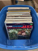 Photo showing multiple vintage vinyl records in a large blue plastic bin. First visible record is 'Pete Fountain & The Village Scramblers Jazz.' Records show minor wear on covers but appear generally in good condition.