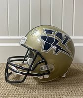 Side view of gold metallic Winnipeg Jets logo football helmet with black facemask, showing a player signature on the helmet's side.