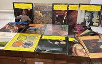 Photo showing a collection of about 15 classical vinyl LPs on a wooden surface. Many have the yellow Deutsche Grammophon label. Visible titles indicate works by Leonard Bernstein, Vivaldi, Berlioz and other notable classical composers. Covers show signs of age but no major damage.
