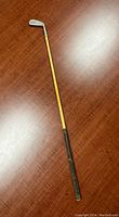 Full length view of the vintage hickory shaft golf club showing the wooden shaft, leather grip and club head.