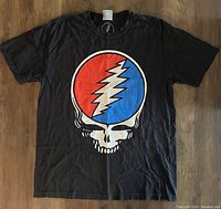 Front view of black Grateful Dead t-shirt with skull and lightning bolt logo on wooden floor.