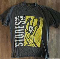 Front of the black cotton T-shirt showing the 94/95 Stones text and yellow abstract illustration.
