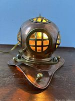 Front and angled view showing the brass and copper divers helmet lamp illuminated, with glass window panes and brass grids visible.