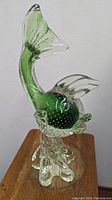 Side view of green Murano glass fish sculpture showing bubble pattern and clear glass base.