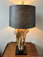 Front view of the driftwood table lamp showing the black drum shade lit from inside, wooden pieces intertwined as base.