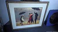 View of the framed art print showing the full gilt decorative frame and white matting inside with the print depicting two couples dancing with umbrellas on a beach.