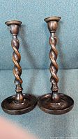 Pair of oak wood barley twist candleholders with metal mounts on top and round wooden base, shown against a blue fabric background.