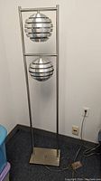 Full view of floor lamp showing tubular frame and two louvered spherical shades