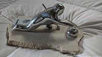 Side angle showing polished metal curler figure with arm extended sliding on raw marble base, with informational card partially visible.