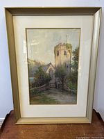 Framed watercolour of an English churchyard with prominent stone church tower and gated path.