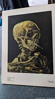 Full view of the vintage macabre art print showing a human skeleton with a cigarette in its mouth on a black background with a white matte board.