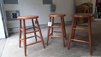 Set of three wooden stools side by side on concrete floor showing overall structure and finish.