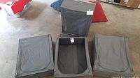Four grey Ikea Skubb underbed storage bins placed on the floor, three closed and one open, showing interior and fabric condition.