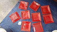 Nine red square plates arranged on blue surface, eight with smooth edges, one with textured edge.