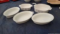 Top view of five oven-safe ceramic bakeware pieces; three oval white dishes, one square, and one rectangular, both with floral patterns.