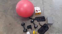 Photo showing pink stability ball, dumbbells, kettlebell, workout gloves, wrist and ankle weights, and a box of hand grips on concrete floor