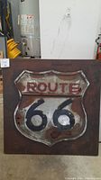 Front view of the rusted 3-D metal Route 66 sign mounted on a rusty background square panel, showing full size and overall condition.