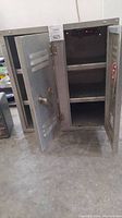 Front view of vintage metal tool cabinet with two open doors showing the interior shelving and latch handle on door.