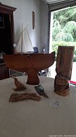 Wooden whale tail fin, tiki statue, small wooden marine animal carvings, driftwood, and glass float on table