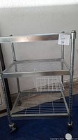 Front view of rolling metal kitchen cart with 3 shelves and casters.