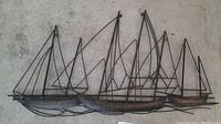 Wide shot of the sailboat metal wall art laid flat on a concrete floor, showing the full piece with multiple sailboats and intricate metalwork.