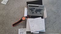 Tommy Bahama watch and world time/alarm clock displayed with original box and manuals on concrete floor.