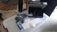 Keyboard and mouse set with can of compressed air and several cords on plastic storage bin lid