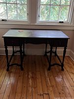 Front view of the antique walnut desk showing the three drawers, turned legs and wooden knob handles.