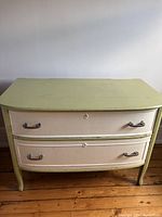 Front view of antique two-drawer dresser painted chartreuse and cream showing metal handles and curved edges.