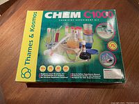 Green box of Thames & Kosmos Chem C1000 Chemistry Experiment Kit showing branding, experiment count, recommended age, and product images.