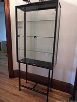 Front view of black metal-framed glass display cabinet with four glass shelves on matching stand