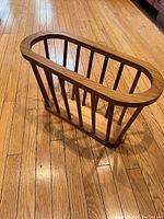 Top side angle view of the solid pine wooden magazine rack showing oval frame and vertical slats on wooden floor.