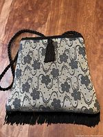 Front view of rectangular beaded purse with floral pattern and tassel on front, black braided strap visible.