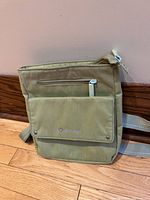 Front view of the green Sherpani purse showing front flap pocket with Sherpani logo and zippered pocket above it.