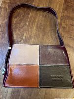 Full view of purse showing front patchwork panels of leather in burgundy, light pinkish beige, orange brown, and dark brown with brand stamped on lower right panel.