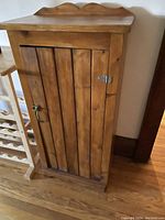 Front view of closed rustic wood cabinet showing vertical slat door with metal latch and handle.