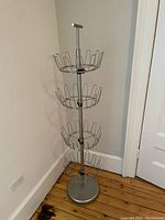 Metal revolving shoe rack with 4 circular tiers designed to hold multiple pairs of shoes, standing in a corner on wooden floor.