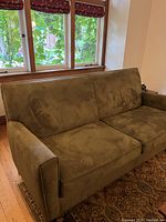 Front angle of olive green fabric sofa showing cushioned seat and backrest, minor lighting variations on fabric.