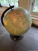 Full view of vintage world globe showing North America on a metal stand by a window lighted area.