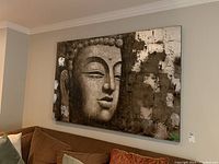 Front-facing photo of large textured Buddha print on wall above couch showing size and texture