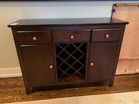 Front view of dark wood cabinet bar showing three drawers, two door storage compartments and central wine rack.