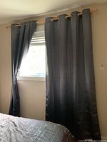 Two dark blackout curtain panels partially drawn closed on a wooden curtain rod above a bedroom window.