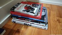 View of seven stacked books on the floor on motorcycle and racing topics, visible titles include BMW Motorcycles, Formula 1 Design, MotoGP, Modern Motorcycle Technology.