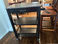 Front view of the wood kitchen cart showing granite top, drawer, two shelves, and wheels